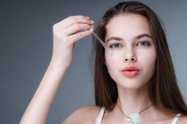 Uzun saçlı çekici bir kız elinde bir serum tutuyor ve bir pipetle yüzüne uyguluyor. Kişisel bakım kavramı