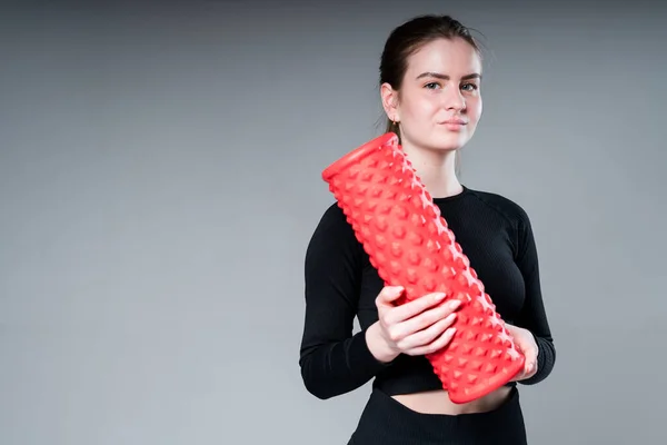 Una hermosa chica con un top negro y polainas sostiene una fascia en sus manos, preparándose para los ejercicios y sonriendo —  Fotos de Stock