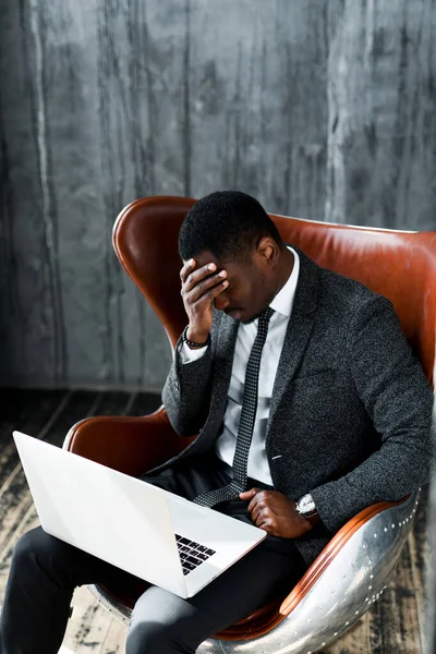 Unavený africký americký kancelářský pracovník dotýkající se jeho čela v důsledku bolesti hlavy při práci na notebooku — Stock fotografie