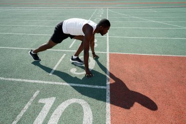 Erkek bir Afrikalı Amerikalı atlet stadyumda bir yarış için hazırlanıyor. Koşu bandının başında