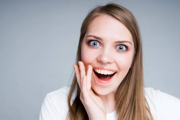 Cute girl in a white T-shirt is surprised opening her mouth and putting her hand to her face — Stock Photo, Image