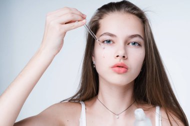 Güzel bir genç kızın portresi deriyle ilgileniyor. Pipetle serumu uyguluyor. Işık arkaplanında izole