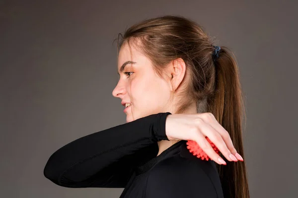 Attractive young girl with a tail and in a black sweater massages the muscles of the back with a massage ball — Foto Stock