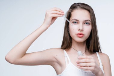 Temiz ciltli güzel bir kız yüzüne pipetle serum sürüyor. Cilt bakımı kavramı