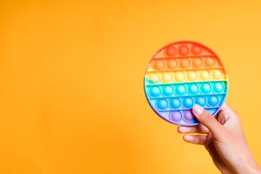 Elin gökkuşağı anti-stres oyuncağını tutarken fotoğrafı sarı arka planda izole edilmiş.