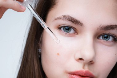 Fotoğrafı kapat. Serum kullanan güzel bir kızın portresi. Yüzünde pipetle serumu sürüp cilt kusurlarından arınıyor.