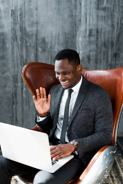 Feliz afroamericano hombre de negocios charlando en skype en el ordenador portátil saludando de la mano y sonriendo — Foto de Stock