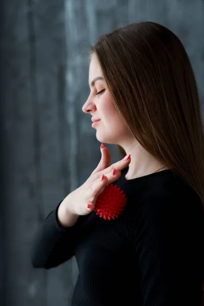 Photo from the side. Beautiful girl in a black sweater, closing her eyes, relaxes the muscles of her chest using a massage ball