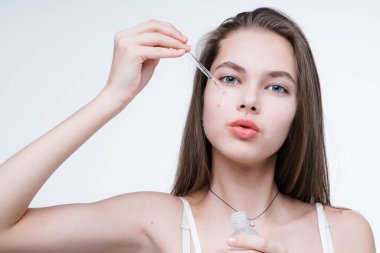 Beyaz tişörtlü çekici genç bir kız kusurlarından kurtulmak için yüzüne bir pipetle serum sürüyor.