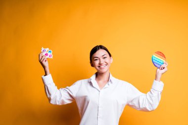 Happy asian girl holding toys pop it and simple dimple in her hands laughing and looking at the camera clipart