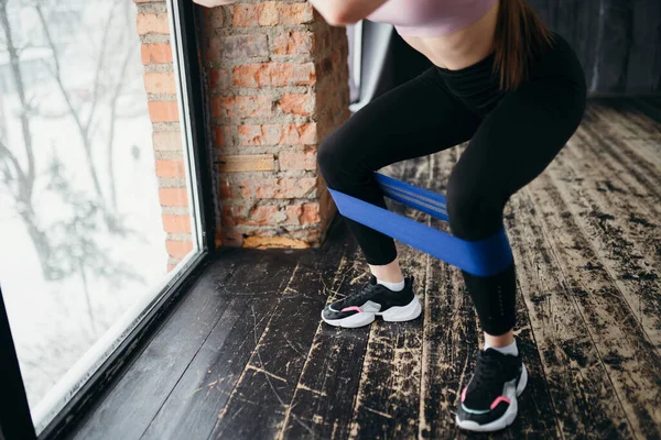 Foto av kvinnliga fötter. Flicka gör knäböj i gymmet med hjälp av ett elastiskt band sträcker den med benen — Stockfoto