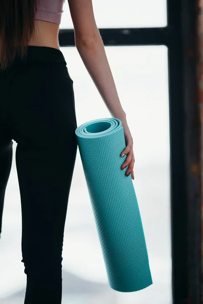 Foto bakifrån. En flicka i svart leggings håller en yogamatta i handen bredvid benen — Stockfoto