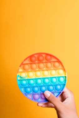 Oyuncak bebek gökkuşağı antistresi tutan kadın el onu sarı arka plana koyar.