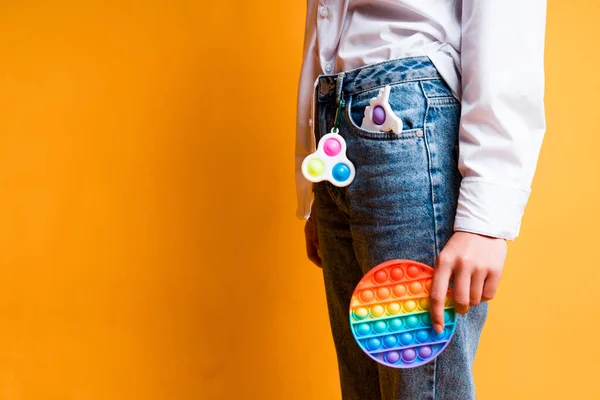 Uma menina de jeans com um simples chaveiro de covinha segura um arco-íris pop-lo brinquedo em sua mão — Fotografia de Stock