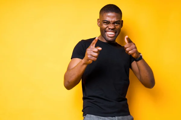 Wesoły, afrykański Amerykanin w czarnej koszulce śmieje się i pokazuje palce przed kamerą uśmiechając się — Zdjęcie stockowe