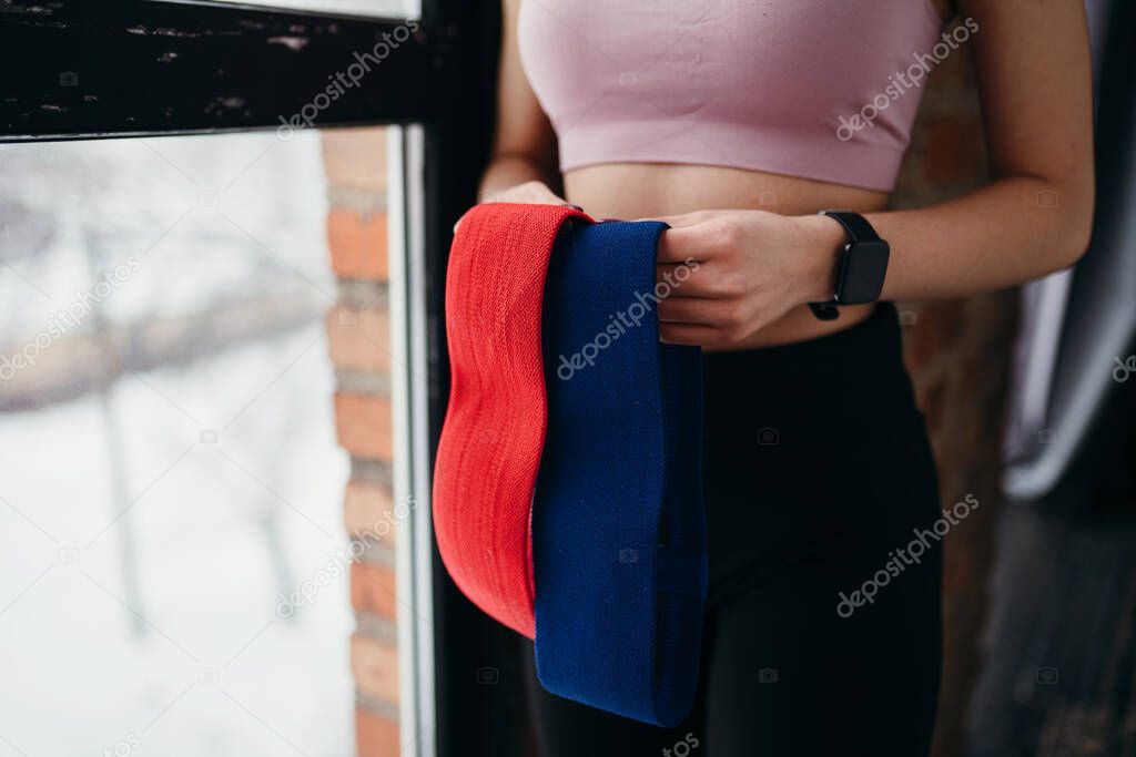 Close up photo. Girl holding multi-colored elastic bands in her hands while standing in the gym