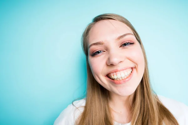Ευτυχισμένο κορίτσι με μακριά μαλλιά χαμογελώντας σε γενικές γραμμές κοιτάζοντας την κάμερα, ενώ στέκεται σε ένα μπλε φόντο — Φωτογραφία Αρχείου