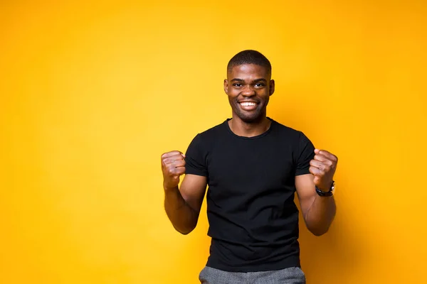 Szczęśliwy, afrykański Amerykanin raduje się zwycięstwem, zaciskając dłonie w pięści i uśmiechając się szeroko. — Zdjęcie stockowe