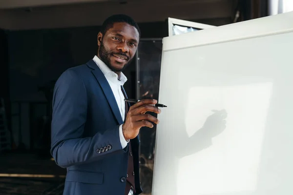 Szczęśliwy afrykański pracownik biurowy prezentuje swój pomysł stojąc przy białej tablicy i uśmiechając się — Zdjęcie stockowe