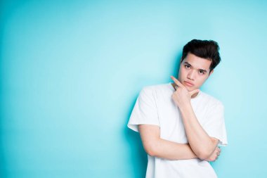 Beyaz tişörtlü havalı genç Asyalı kameraya bakarken yan tarafı gösteriyor.