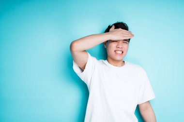 Yakışıklı Asyalı adam başarısız olurken elini alnına vuruyor. Mavi arkaplanda izole