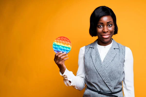 Beautiful cute african american girl holding a childrens toy intistress rainbow pop it smiling and looking at the camera — Stock Photo, Image