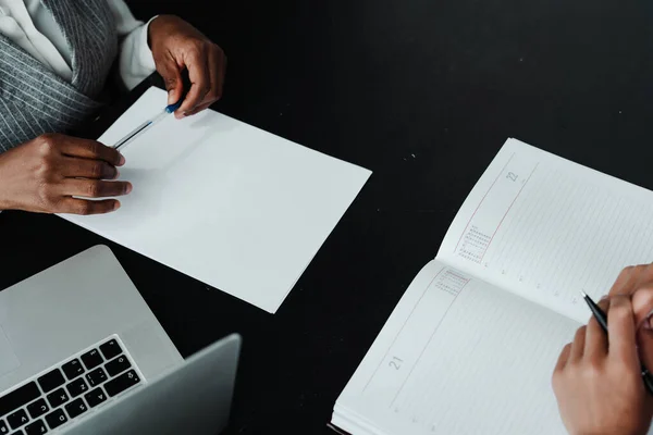 Foto von oben. Weibliche Hände halten Stifte, während sie am Tisch neben einem Laptop Papiere und Dokumente ausfüllen — Stockfoto