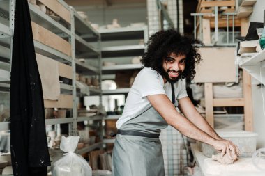 Önlüklü yakışıklı Afro-Amerikalı adam kil heykeller yapıyor ve çatal bıçak yapmak için hazırlıyor.