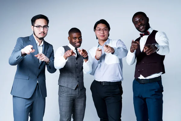 Afričtí američtí a asijští podnikatelé v oblecích s úsměvem a ukazující na fotoaparát, zatímco stojí na lehkém pozadí — Stock fotografie