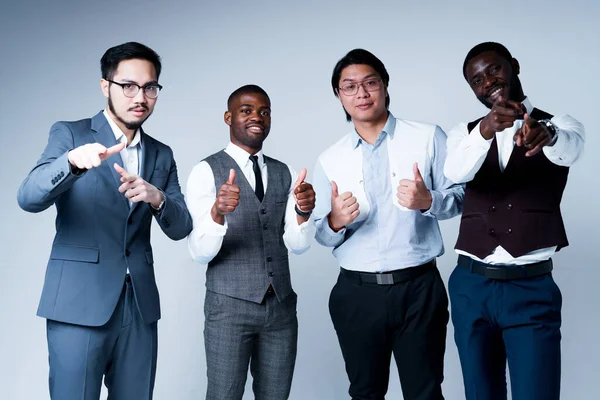 Skupina afrických amerických a asijských podnikatelů v oblecích ukazuje prsty na fotoaparát a palce nahoru — Stock fotografie