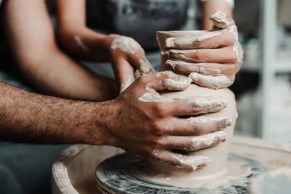 Photo du côté. Les mains d'un mec et d'une fille font un vase d'argile sur une roue de potiers — Photo