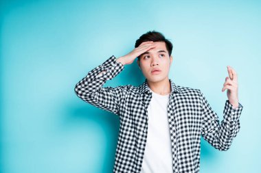 Odaklanmış Asyalı bir adam ateşini ölçmek için alnına dokunur ve hastalanmamak için dua eder.