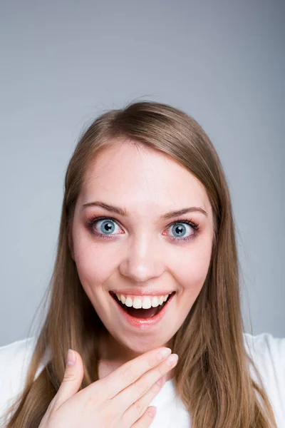 Retrato de uma linda garota olhando para a câmera de surpresa ao abrir a boca e aplicar a mão na boca — Fotografia de Stock