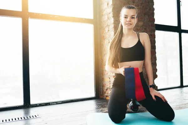 Fată de sport în studioul de fitness stă pe mat și deține trupe elastice pentru întindere — Fotografie, imagine de stoc