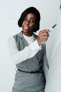 Çekici Afro-Amerikan kadın öğretmen beyaz tahtaya kalemle çiziyor ve ders konusunu anlatıyor.