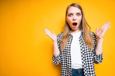 Ekose gömlekli tatlı bir kız şaşırır ve ağzını açarken ellerini açar.