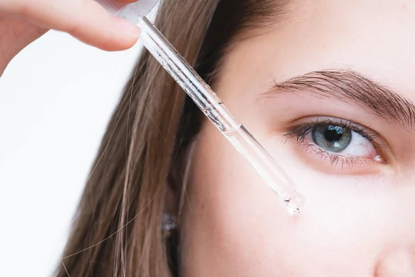 Närbild. Flickan applicerar ett serum på huden runt ögonen samtidigt som hon håller en dropper med handen — Stockfoto