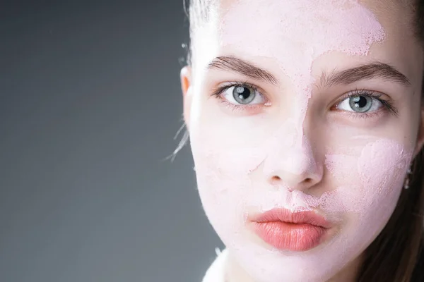 Retrato de una hermosa chica con una máscara de arcilla púrpura en su cara. Aislado sobre fondo gris — Foto de Stock