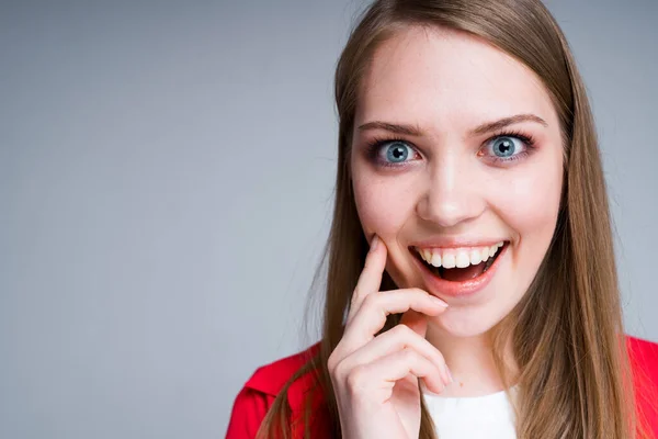 Menina bonita feliz com olhos azuis abre a boca em surpresa, tocando seu queixo com o dedo — Fotografia de Stock