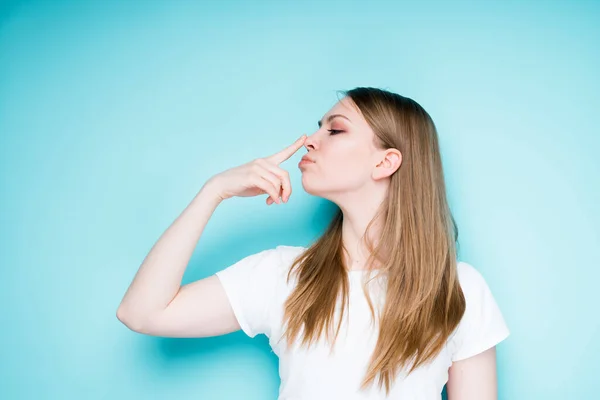 Attrayant jeune fille toucher son nez avec son doigt de plaisanterie autour et jouer tout en se tenant debout sur un fond bleu — Photo