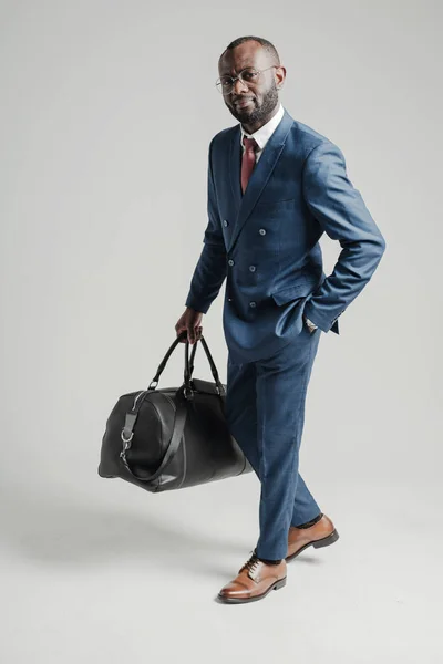 Afroamerykanin biznesmen w garniturze trzyma torbę z rzeczami w ręku i jedzie w podróż służbową — Zdjęcie stockowe