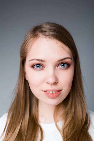 Retrato de una hermosa jovencita coqueteando y mirando a la cámara mientras está de pie sobre un fondo gris — Foto de Stock