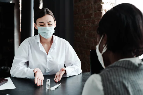 Cute asian girl doctor in medical mask offers vaccine to african american woman