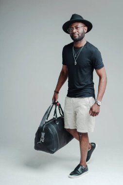 Şapkalı, bavul taşıyan yakışıklı Afro-Amerikan turist. Turizm konsepti