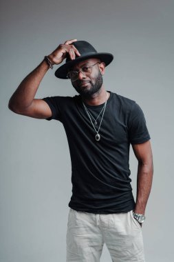 Tişörtlü, eli cebinde ve şapkası elinde tutan yakışıklı Afro-Amerikan bir adam.