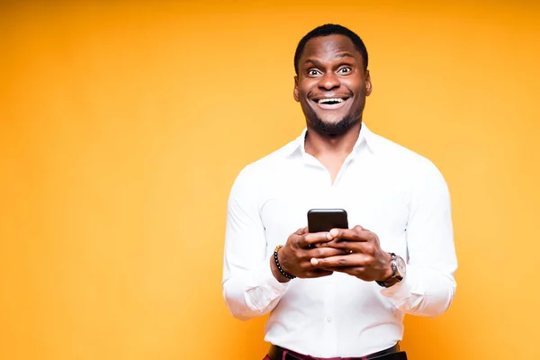 Красивый счастливый африканский американец держит телефон в руке и улыбается, глядя в камеру. — стоковое фото