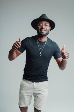 Şapkalı ve yaz kıyafetli neşeli Afro-Amerikalı adam başparmağını kaldırıp gülümsüyor.