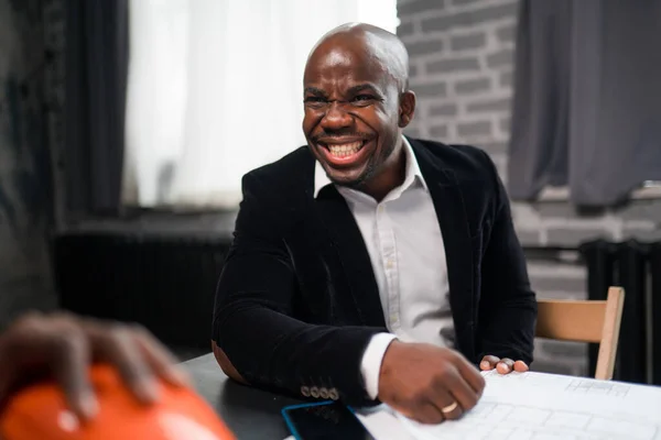 Empresário americano africano feliz de terno rindo enquanto sentado à mesa em negociações — Fotografia de Stock