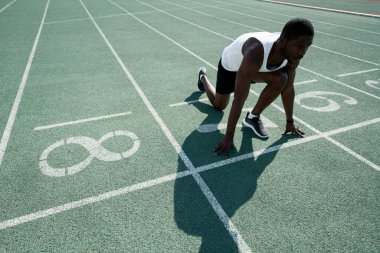 Afrika kökenli Amerikalı erkek sporcu, yarışın başında ayakta dururken yarışa hazırlanıyor. Etkin yarışmalar