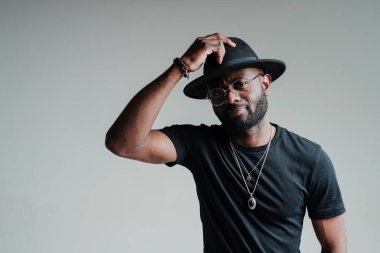 Gözlüklü ve şapkalı yakışıklı Afro-Amerikan adam ona dokunuyor. Gülümsüyor ve gri bir arka planda duruyor.